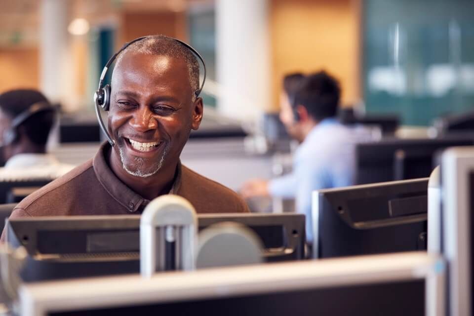 Person smiles while looking towards their monitor, wearing a headset