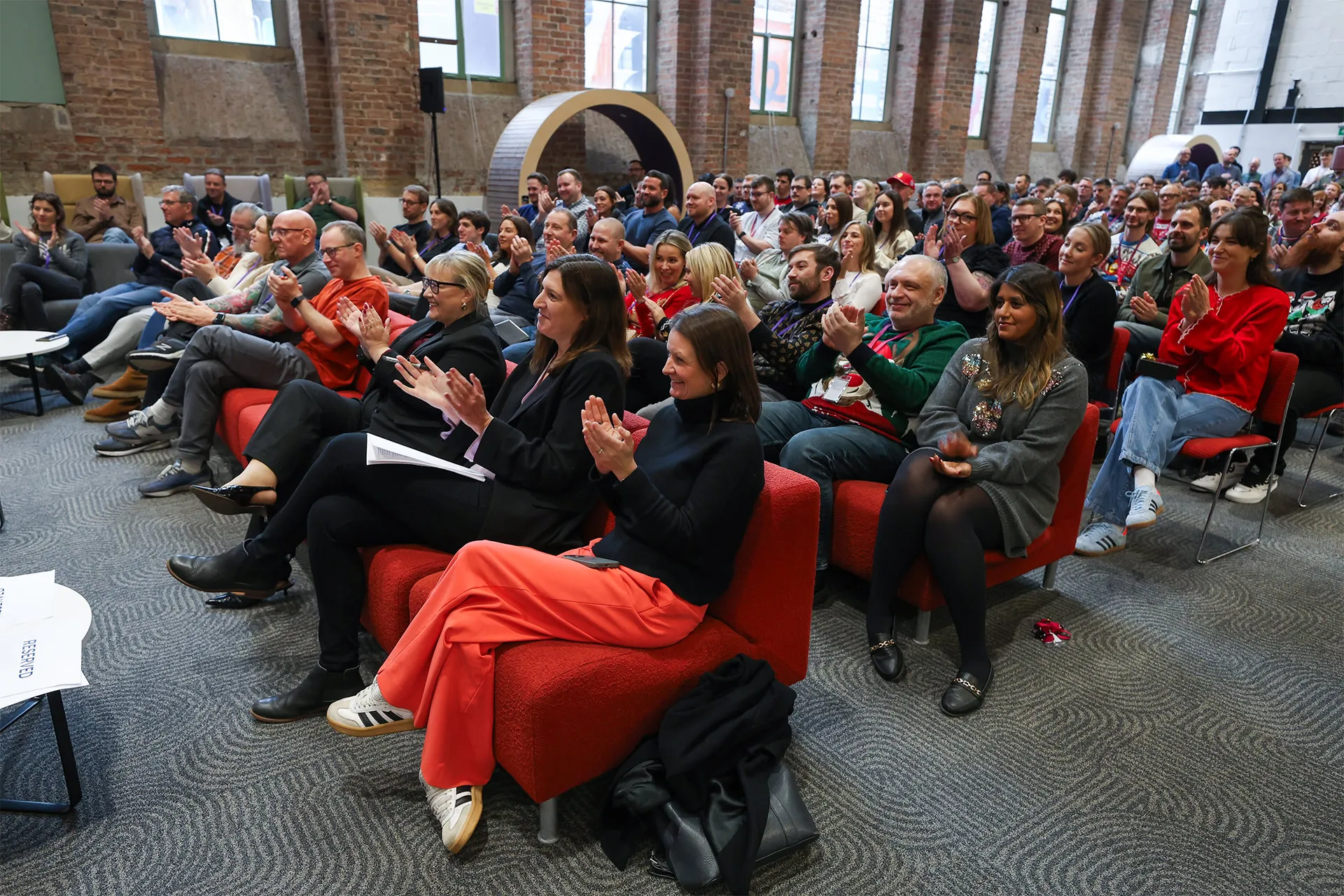 A large group of people sitting on chairs in a hall clapping their hands