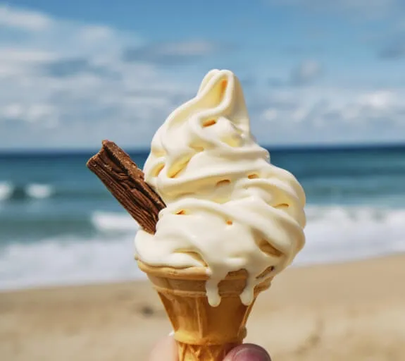 Someone holding a soft serve ice cream cone with a flake at the beach. The copy Atomic numbers Summer 2021