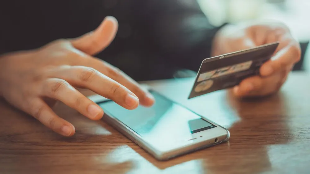 A person holding their credit card and paying for something on their phone