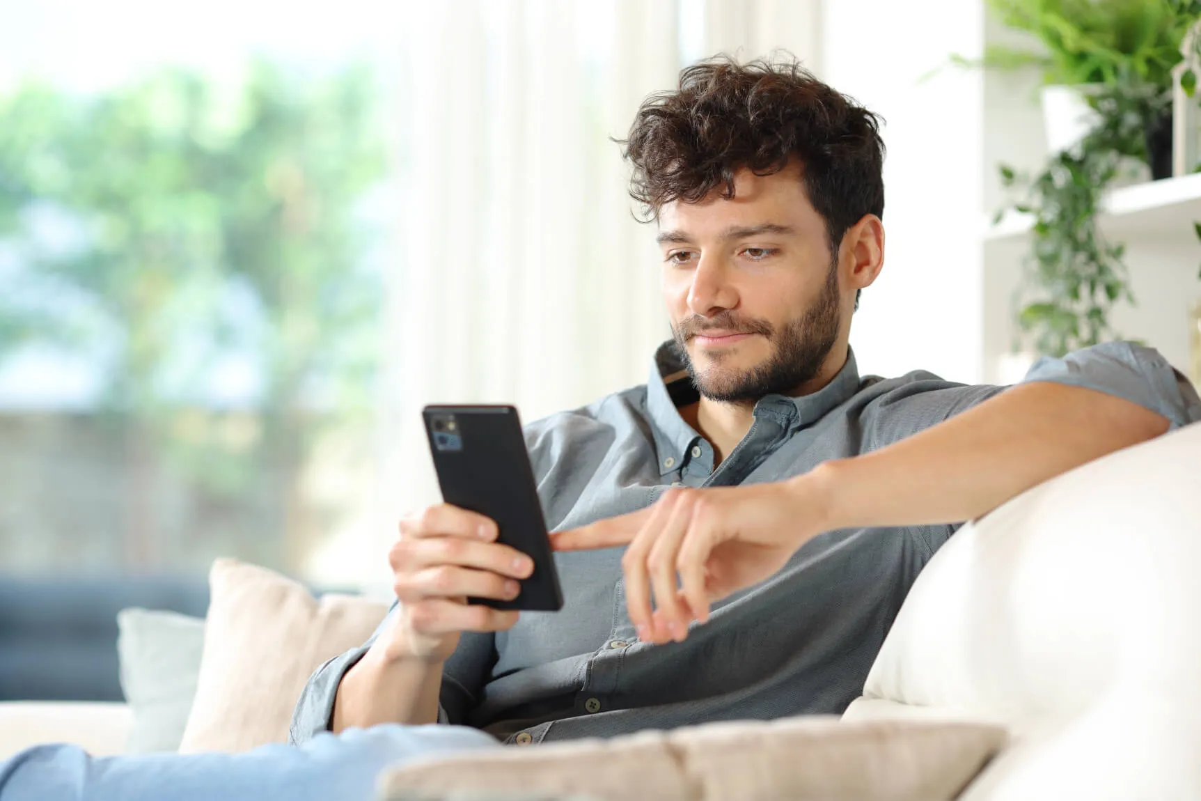 A man sitting on the sofa holding his phone and scrolling