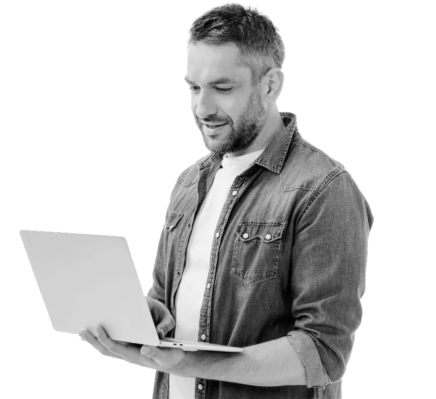 A man is standing and holding his laptop in one hand as he types on the keyboard with the other hand