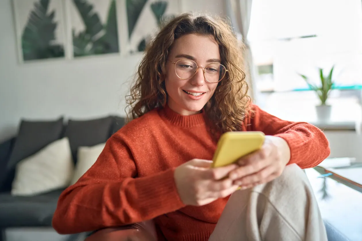 Girl wearing orange jumper sitting down looking at her phone and smiling