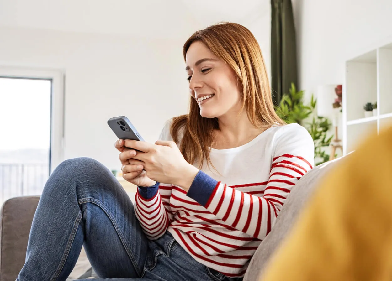a woman smiling whilst sitting on the sofa using her phone