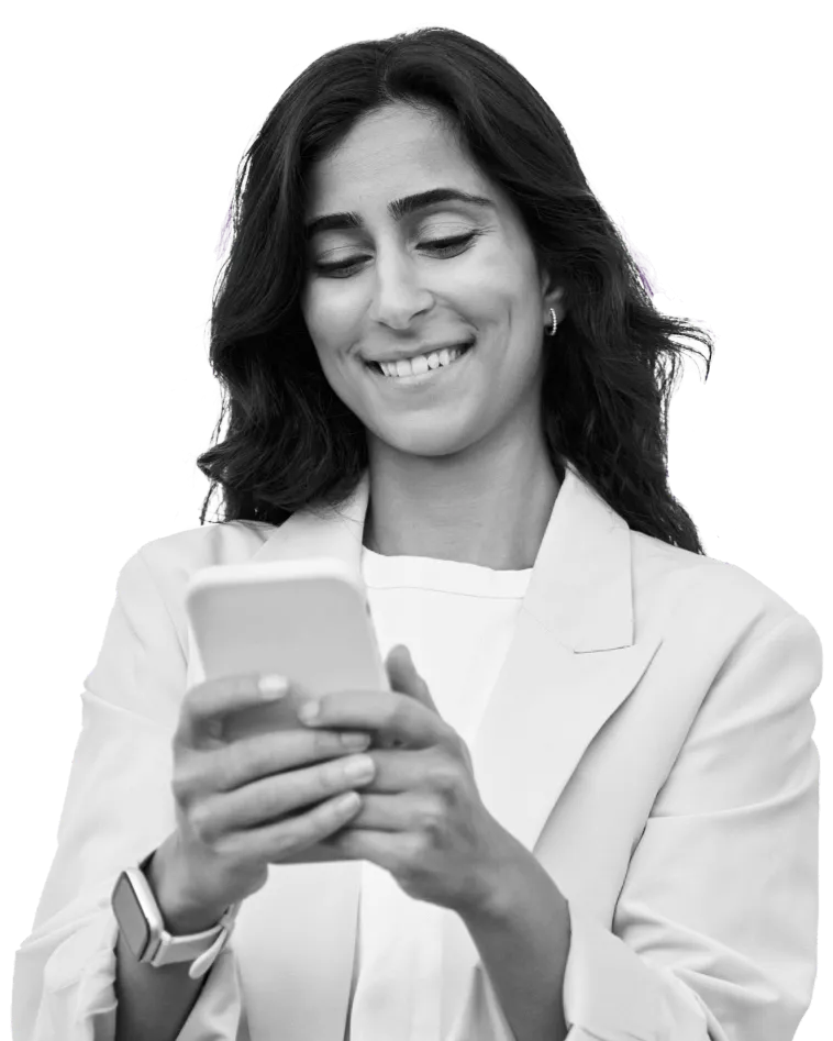 A smiling woman wearing a blazer looking down at the phone in her hands.