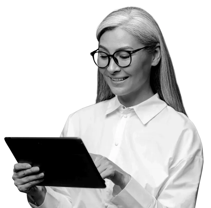 A woman wearing glasses is smiling whilst looking down at her tablet