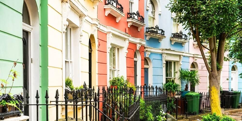 Brightly coloured row of terrace houses in a curve. All featuring black cast iron railings with steps up to the front door