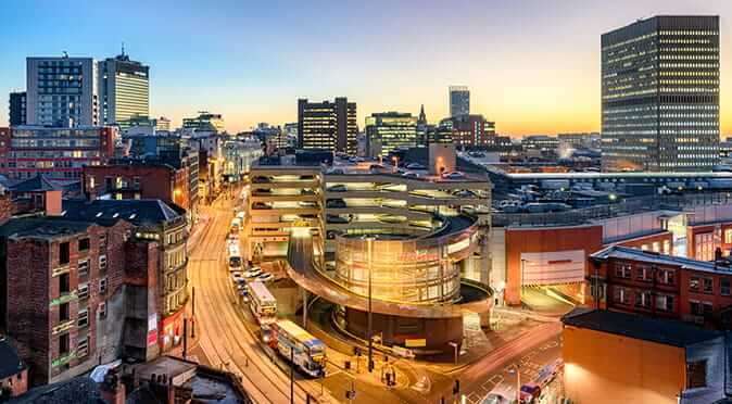 Manchester city skyline at sunset overlooking a multi-story car park and mix of old and new buildings