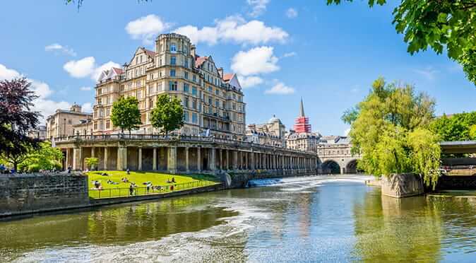 Bath city riverside during the summer with lush green trees and grass, bridges and old, beautiful buildings