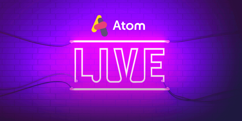 A dark scene where a brick wall is illuminated by a pink neon sign spelling out LIVE with the Atom Bank logo above it