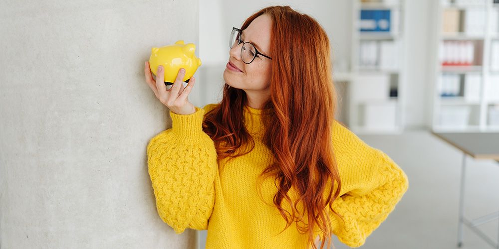 A women in a yellow jumper holding a yellow piggybank