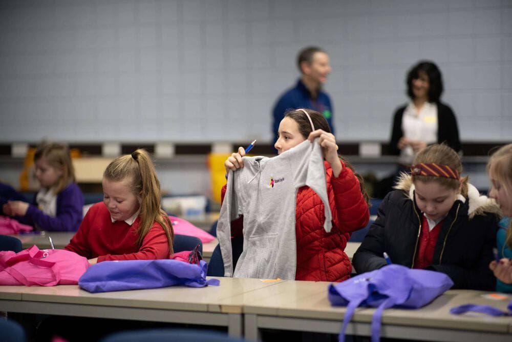 Girl in red coat, holding up her gifted Atom bank hoody