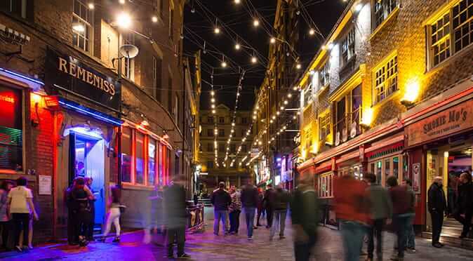 Busy Liverpool street of bars and clubs, with glowing overhead lights and a buzz of people
