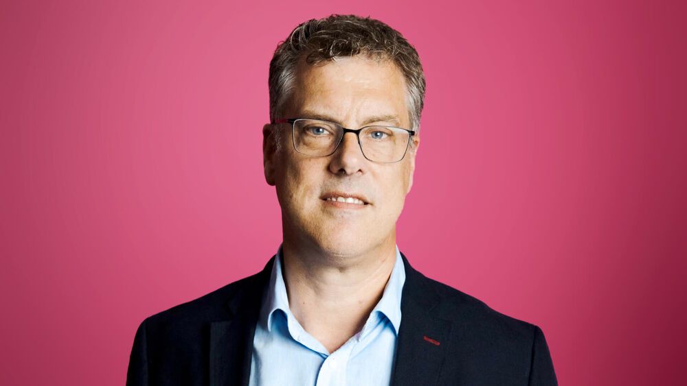 A photo head shot of David McCarthy infront of a pinkish-red background