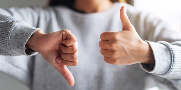 Woman wearing a grey sweater holding one thumb up and one thumb down in front of her