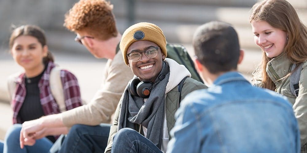 Group of five students sat together laughing and talking on their campus stairs