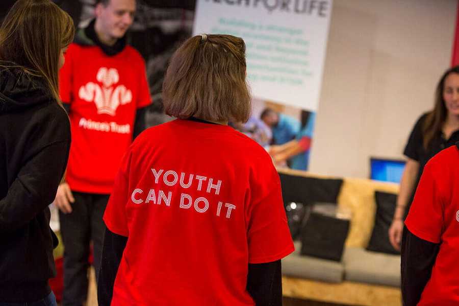 Group of young people stood in a circle wearing Princes Trust red tshirts with the phrase Youth can do it on the back