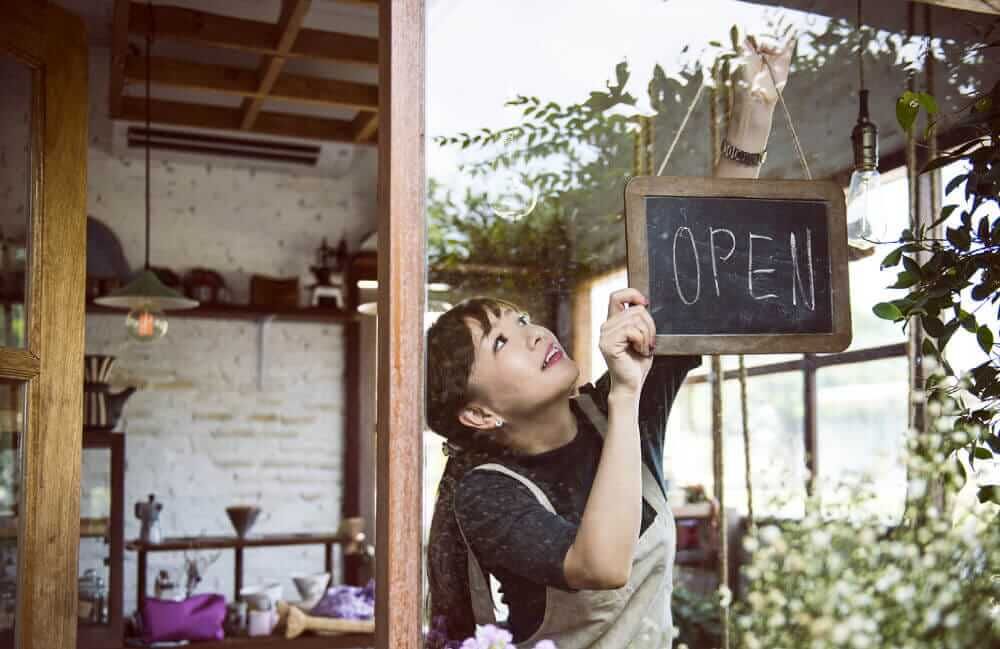 Woman wearing apron in coffee shop window hanging and open sign