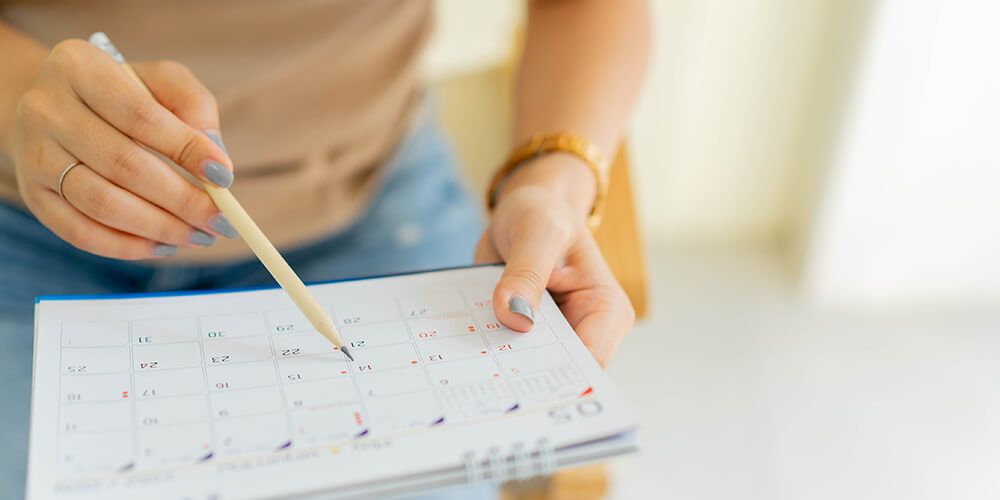 Woman's hands are shown. She is using a pencil to mark a date on a small calendar