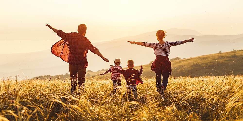 Family of four running through fields of wheat with their arms wise as the sun starts to set