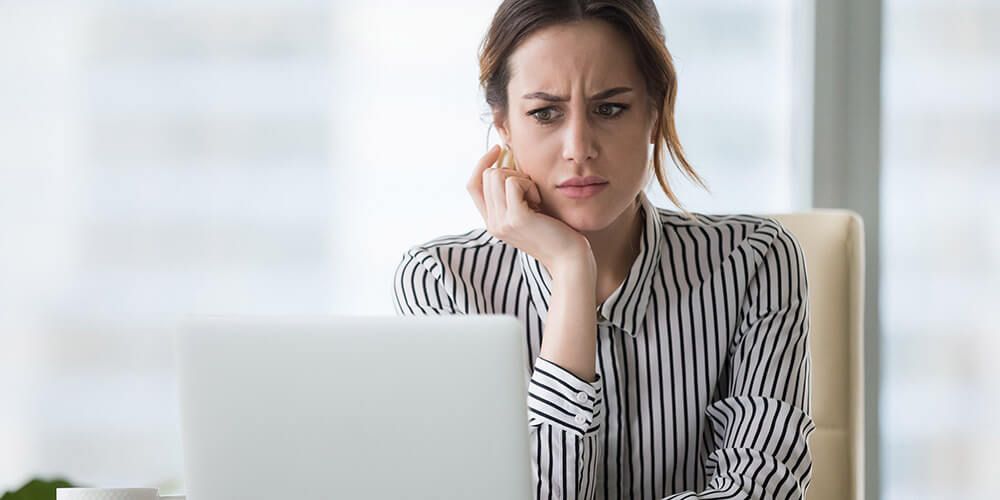 A woman looking at a laptop screen with an anxious, stressed look on her face