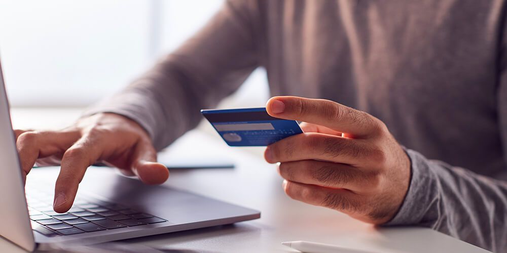 A person holding a bank card while entering details into a laptop keyboard