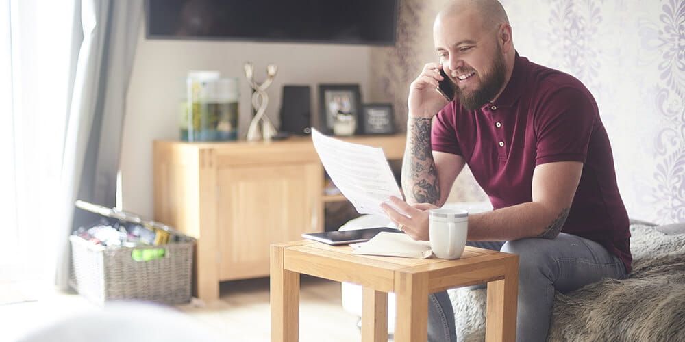 Bald man with beard smiling whilst on the phone and reading a piece of paper displaying his Atom bank mortgage letter