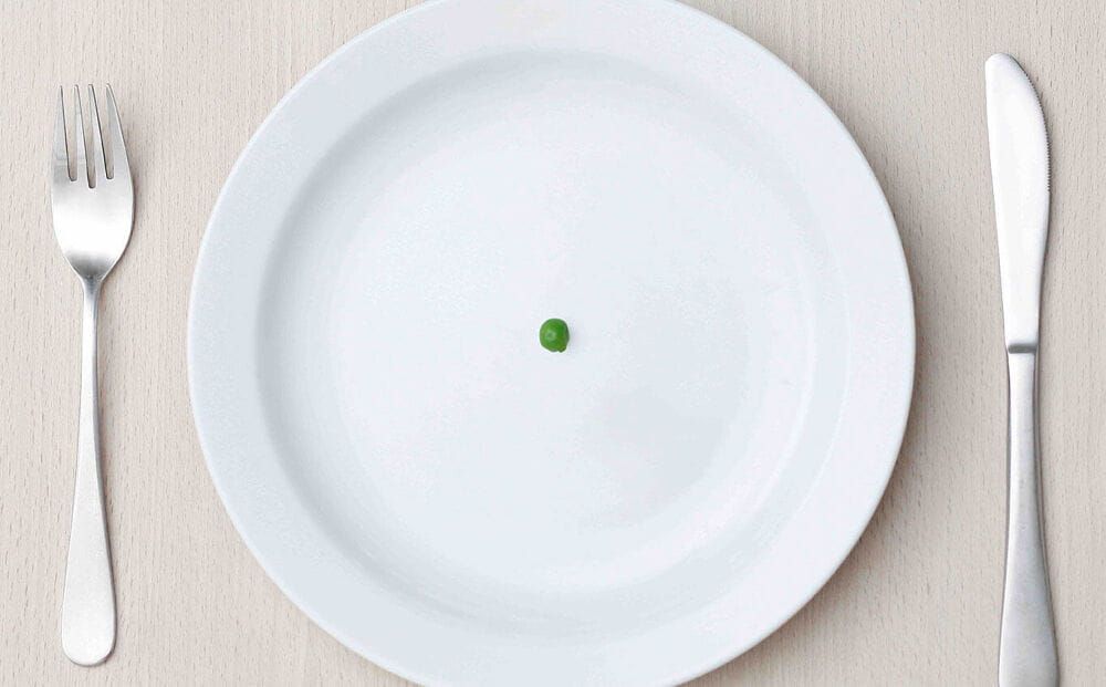 Over head shot of a single green pea in the centre of a white plate