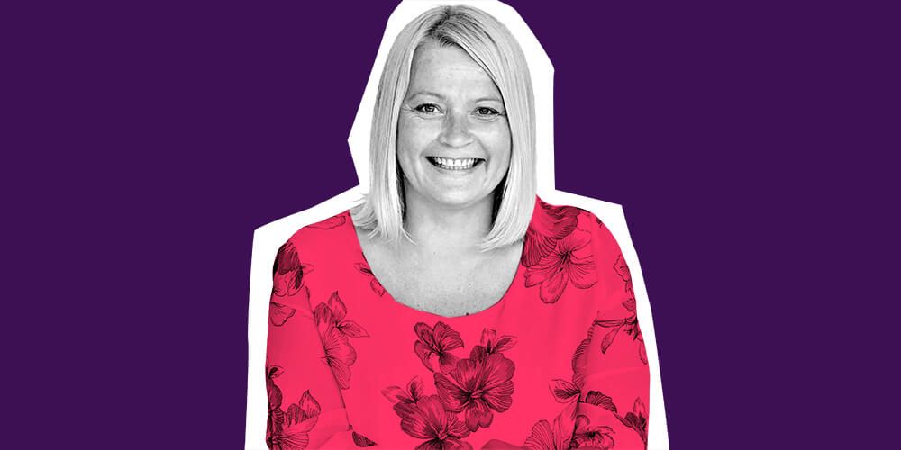 Atom bank employee smiling wearing a pink top with large flowers on it, against a purple background