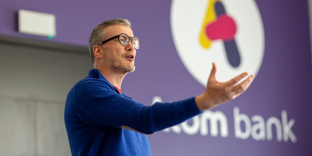 Atom bank CEO, Mark Mullen, wearing glasses and a blue sweater whilst presenting at the Atom HQ