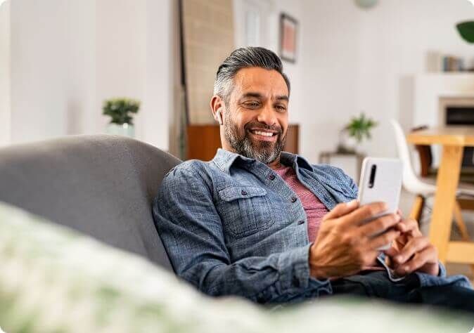 A person slouched on a sofa looking at their phone and smiling