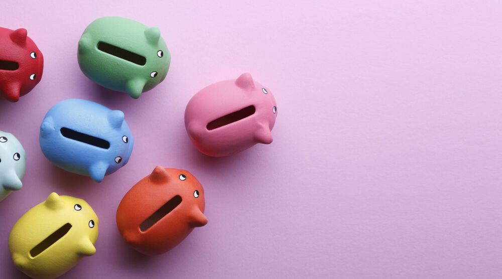 A collection of different brightly coloured piggy banks, seemling walking in a triangle formation across a pink table