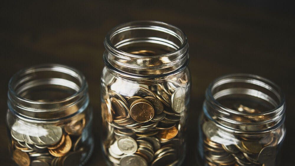 Three jars being used as savings pots full of pennies and copper coins
