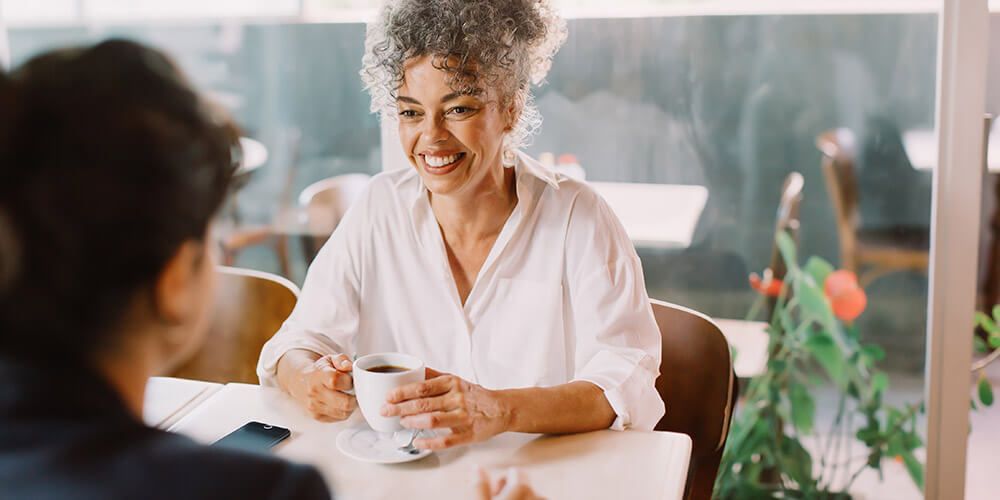 A lady enjoying a coffee break while talking to a colleague