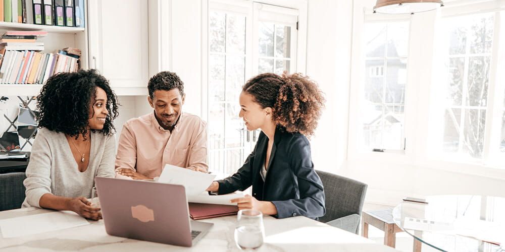 A man and a woman speaking to their mortgage broker whilst reading off a piece of paper and a laptop